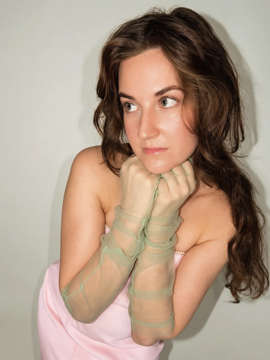 A close-up portrait looking to the side in a pink look with sheer sage-green gloves.