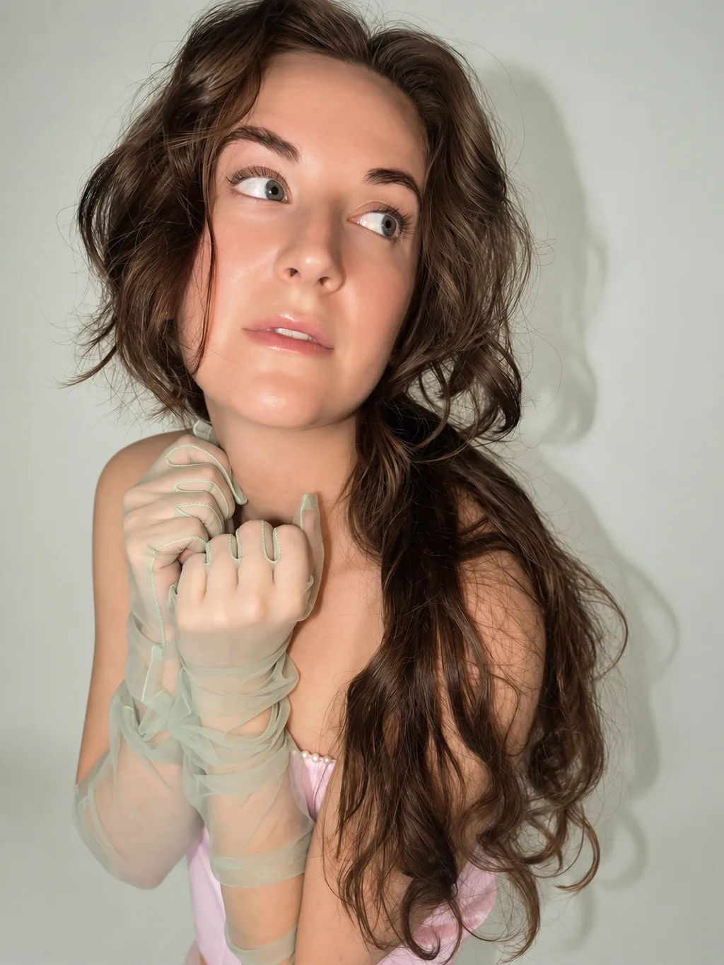 A close-up portrait with hands gathered beneath the chin in sheer sage-green gloves.