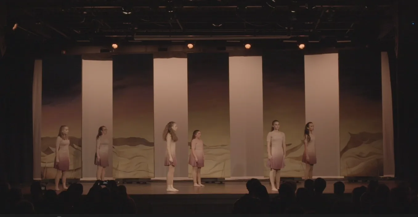 The backdrop onstage behind white panels, lit so the sandy landscape glows and the sky recedes.