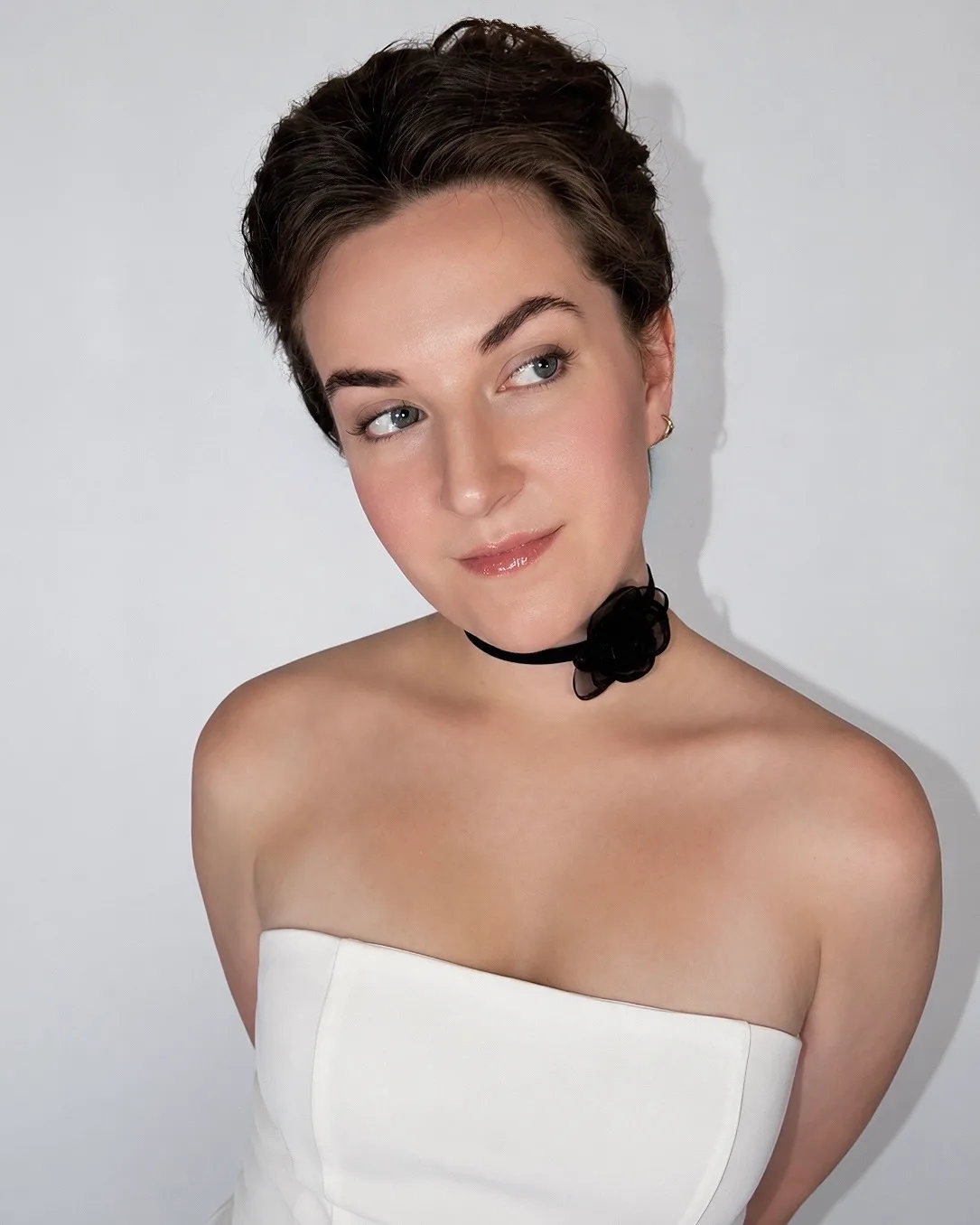 A portrait in a structured white dress with a black floral choker.
