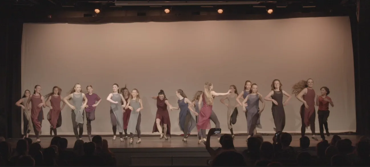 A large ensemble in a line across the stage under bright light.