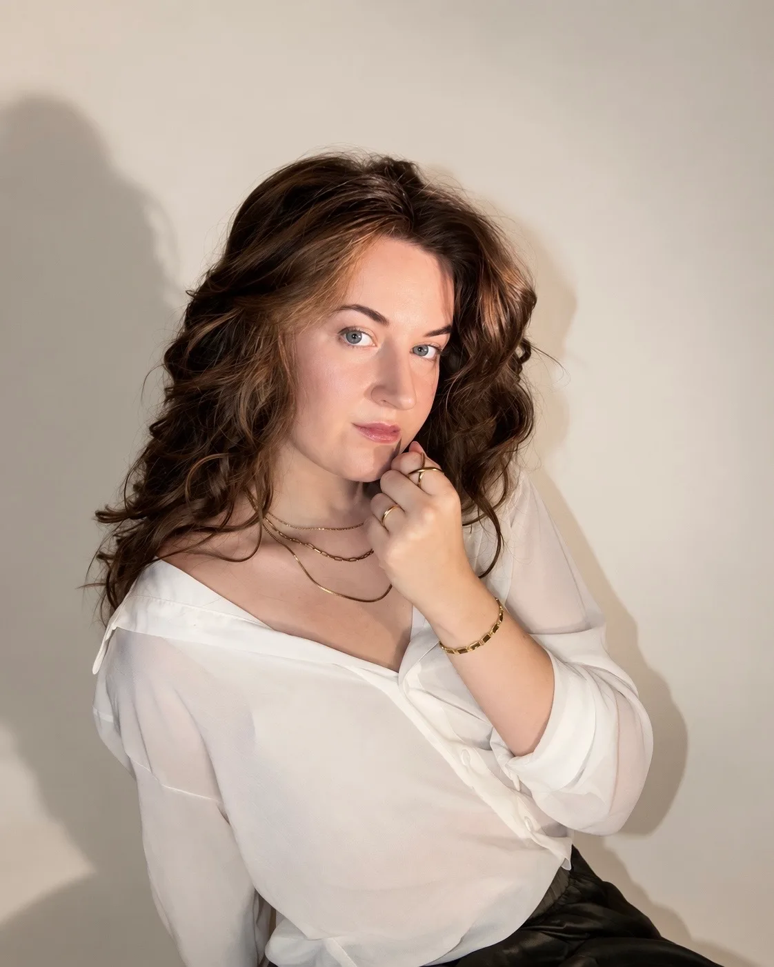 Close portrait in a white blouse with layered gold necklaces, lit by warm directional light.