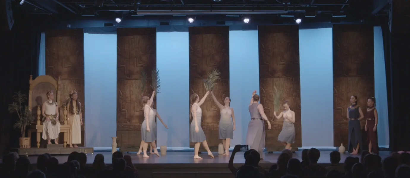 Dancers in white on a palace set lit in pale blue, with a golden throne at stage left.