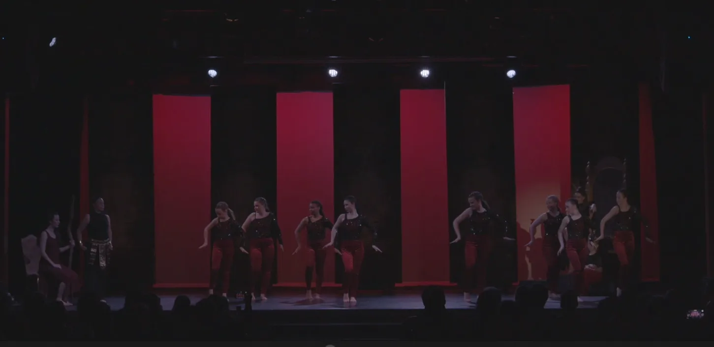 Dancers in dark costumes against deep red panels.