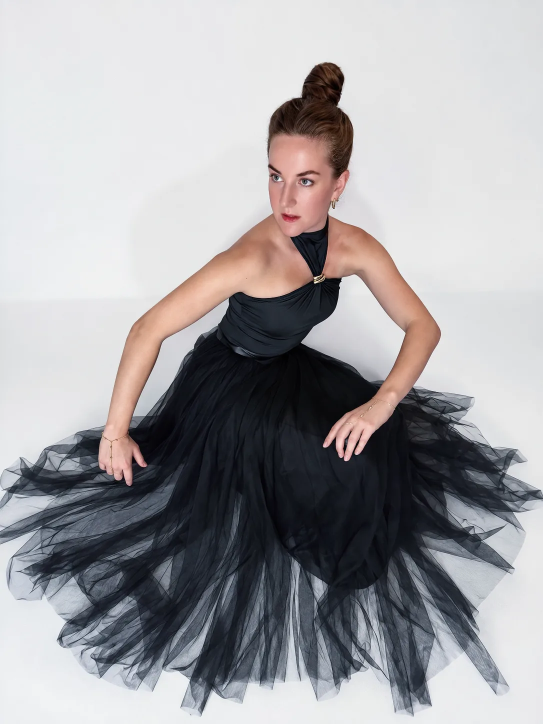 A woman seated in a black tulle dress against a pale backdrop.