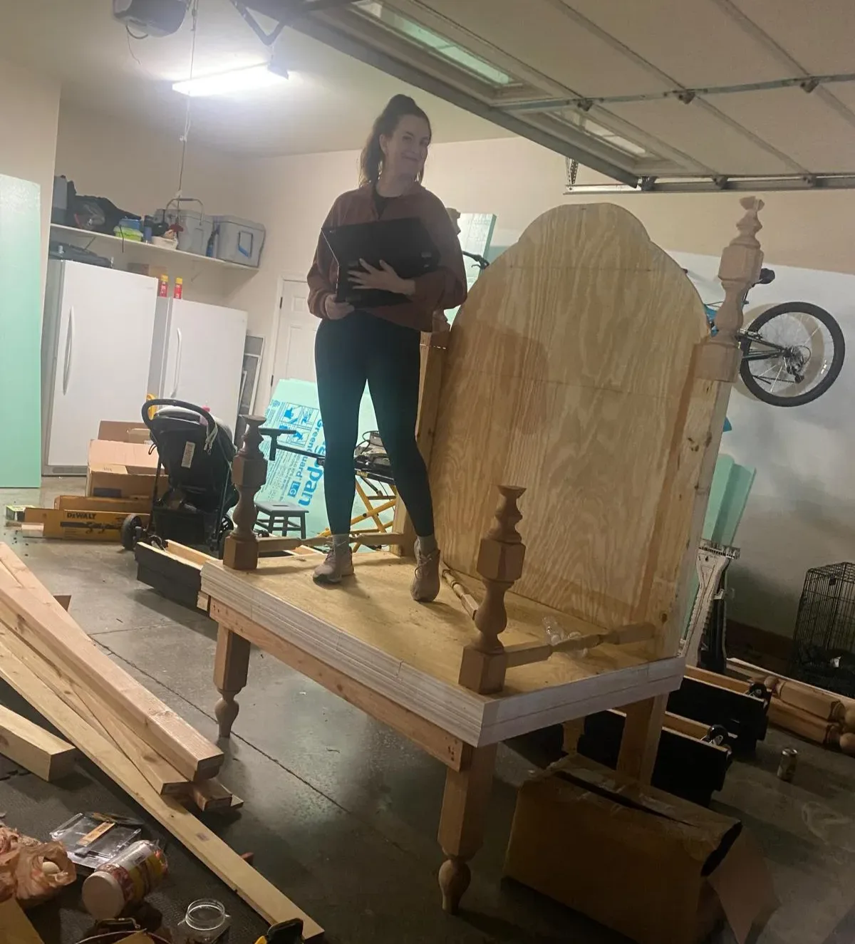A person standing beside the unfinished wooden throne in a workshop.